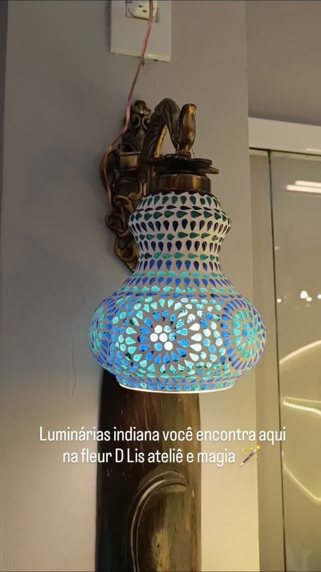 Luminária indiana de mosaico azul e verde presa na parede por um suporte de metal trabalhado